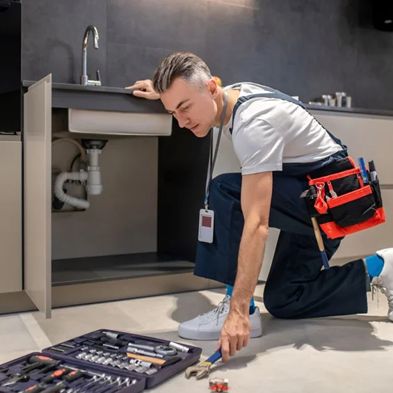 Plumber with toolbox repairing sink, representing seamless handyman services