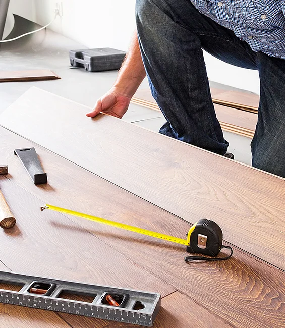 Close-up of a person measuring wooden planks for precise flooring installation with tools on a table.