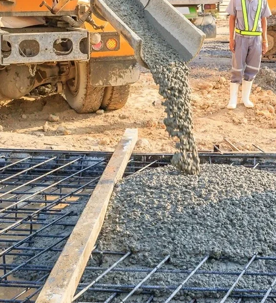 Concrete being poured from a cement truck onto a steel-reinforced foundation at a construction site.